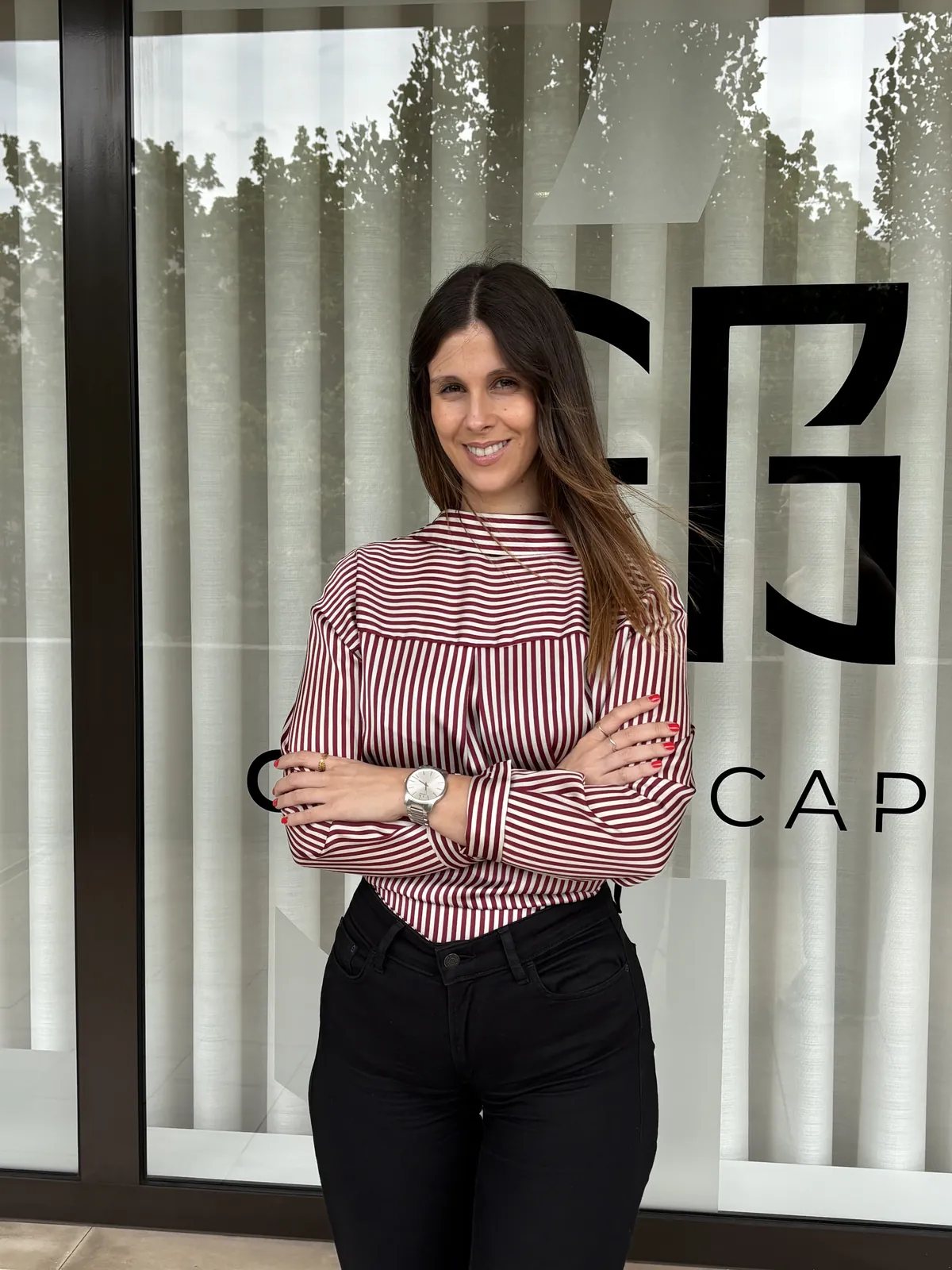 Colaboradora da Classe Capital, de braços cruzados e a sorrir, diante da montra do escritório com o logótipo