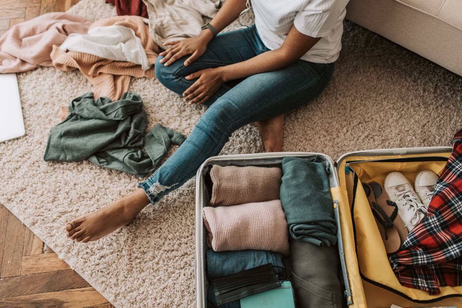 Mala de viagem aberta com roupa dobrada, junto a uma pessoa sentada no chão
